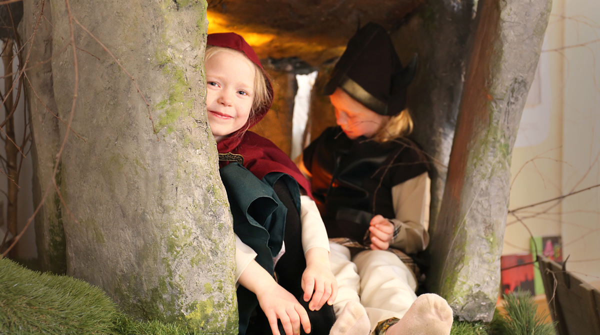 Två barn i medeltidskläder sitter i utställningens grotta